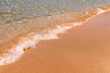 Transparent sea water. The golden sand is washed by small waves of clear water with foam. Marine background. tourism and travel