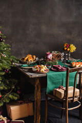 Stylish table setting for christmas family dinner with christmas tree on the background and gifts on the chair.