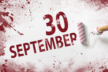 September 30th. Day 30 of month, Calendar date. The hand holds a roller with red paint and writes a calendar date on a white background. Autumn month, day of the year concept.