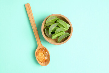 Spoon with aloe gel and bowl with slices on mint background