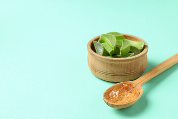 Spoon with aloe gel and bowl with slices on mint background