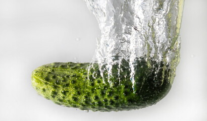 green cucumber falls into the water scattering a lot of sprays and drops