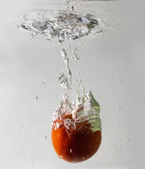 Ripe tomato falls deeply under water with a big splash