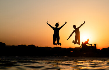 Joyful friends are having fun and jump at sunset beach in sunlight. Empty space for text