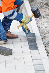 A worker lays down paving slabs with a rubber hammer on a pedestrian stretch of sidewalk. Vertical image.