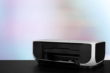 Compact laser printer on black desk against blurred background