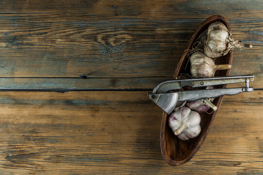 Organic garlic with metal press. Fresh garlic cloves and garlic bulb on a wooden table. Garlic for healthy eating. Concept of spices for healthy cooking. Closeup