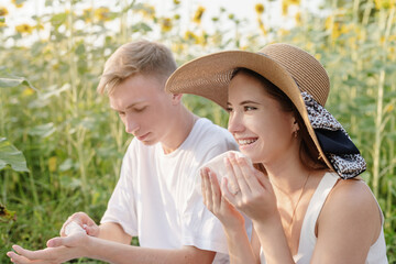 Young couple having picnic on sunflower field at sunset, wiping their hands and faces
