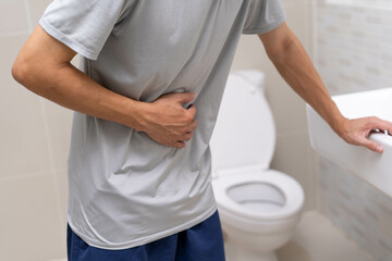 A man standing has diarrhea and severely toxic food. Man touch belly in the bathroom. Abdominal...