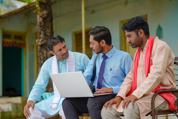 Young indian banker or agronomist showing some detail to farmers in laptop at home