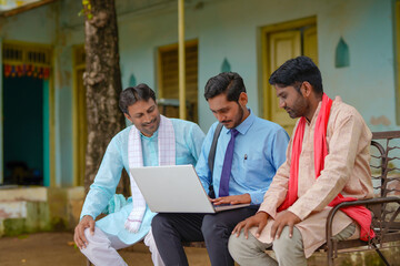 Young indian banker or agronomist showing some detail to farmers in laptop at home