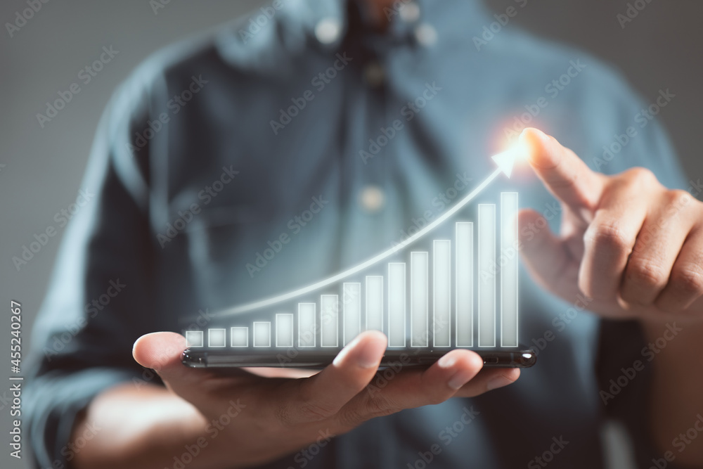 Fototapete Business man holds a mobile phone and displays a graphic graph showing statistics of profitable graphs, ideas of growth planning and business strategy to see trends in good business.