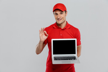 Young delivery man in uniform gesturing while showing laptop