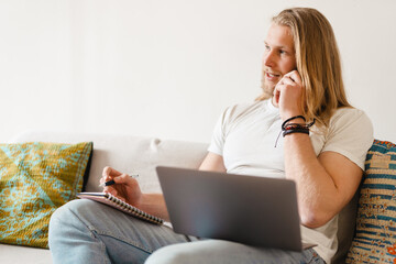 Fototapeta premium Bearded blonde man talking on cellphone while working with laptop