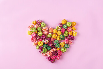 Love movies concept. Colorful rainbow caramel candy Popcorn scattered on pink background, heart shaped close up, copy space for text. Cinema snack concep