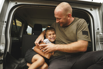 Happy father and son sitting in car trunk