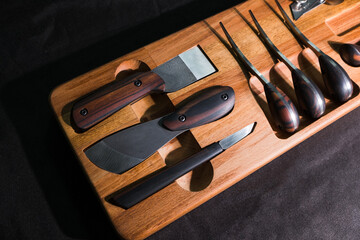 Exclusive handmade leather craft tools. Close up of different tanner tools on wooden box. Set of Different knifes from steel and wood. Black background.