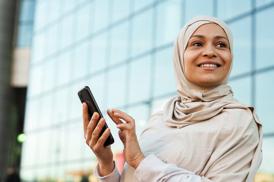 Middle Eastern Woman In Hijab Smiling While Using Mobile Phone