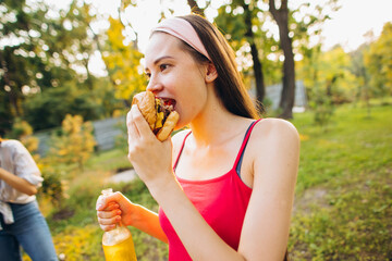 Cropped image of young joyful girl eating burger on warm summer day picnic