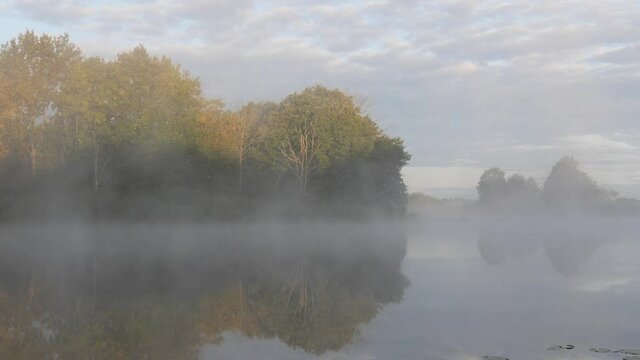 morning fog spreads over the smooth water of the river