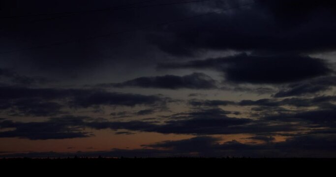 Time-lapse of fast moving dramatic clouds on sky at sunset over forest horizon. From dusk to darkness 