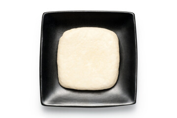 A piece of fresh tofu on a black plate on white backgorund.