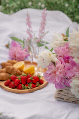 Outdoor picnic with champagne, strawberries, croissants and a bouquet of peonies
