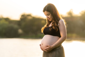 Pregnant woman looking and touching her belly while standing in a park
