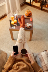 halloween, holidays and leisure concept - young woman using smartphone at home