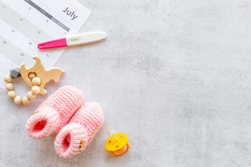 Pregnancy test with pink baby girl booties and calendar, top view