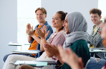 Portrait of cheerful university student sitting and studying in classroom indoors, clapping.