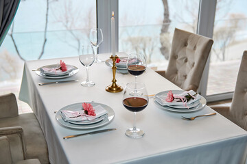 A decorated restaurant table with glasses of red wine and lighted candle awaits guests. Close-up, selective focus