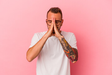 Young caucasian man with tattoos isolated on pink background  holding hands in pray near mouth, feels confident.