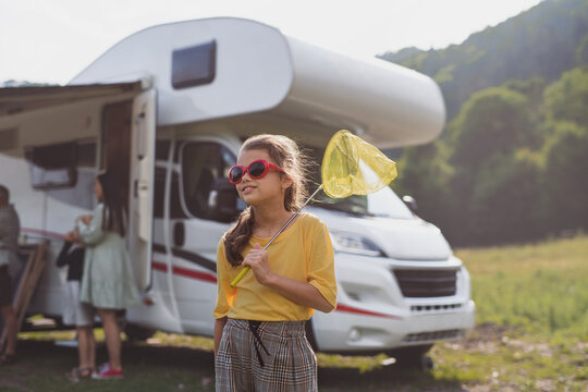 Happy small girl with sunglasses standing outdoors by caravan car, family holiday trip.