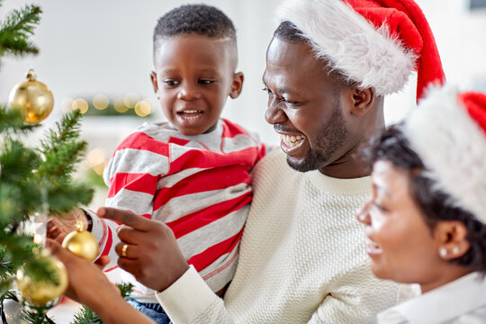 family, winter holidays and people concept - happy african american mother, father and little son decorating christmas tree at home on