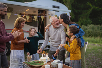 Senior man celebrating birthday outdoors at campsite, multi-generation family caravan holiday trip.