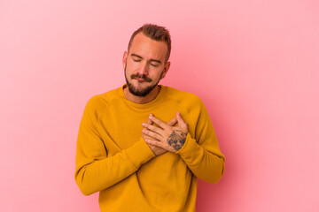 Fototapeta premium Young caucasian man with tattoos isolated on pink background has friendly expression, pressing palm to chest. Love concept.