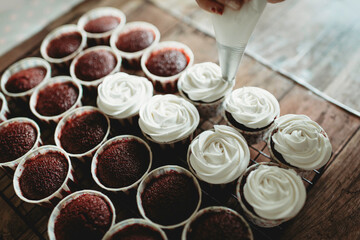 White cream on red velvet cupcakes.Piping on cup cakes.Step by step process of cake decorating with icing.Baking and culinary preparation.