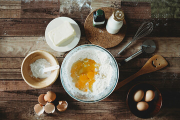 Baking ingredients on wooden table.Healthy homemade recipe for breakfast.Pastry and culinary.Flour and egg yolks in glass bowl.Milk bottle, whisker and butter.Home bake space.Pizza dough.