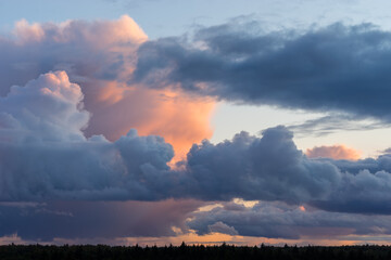 Beautiful colored dramatic stormy cumulus clouds on sky at sunset over forest horizon
