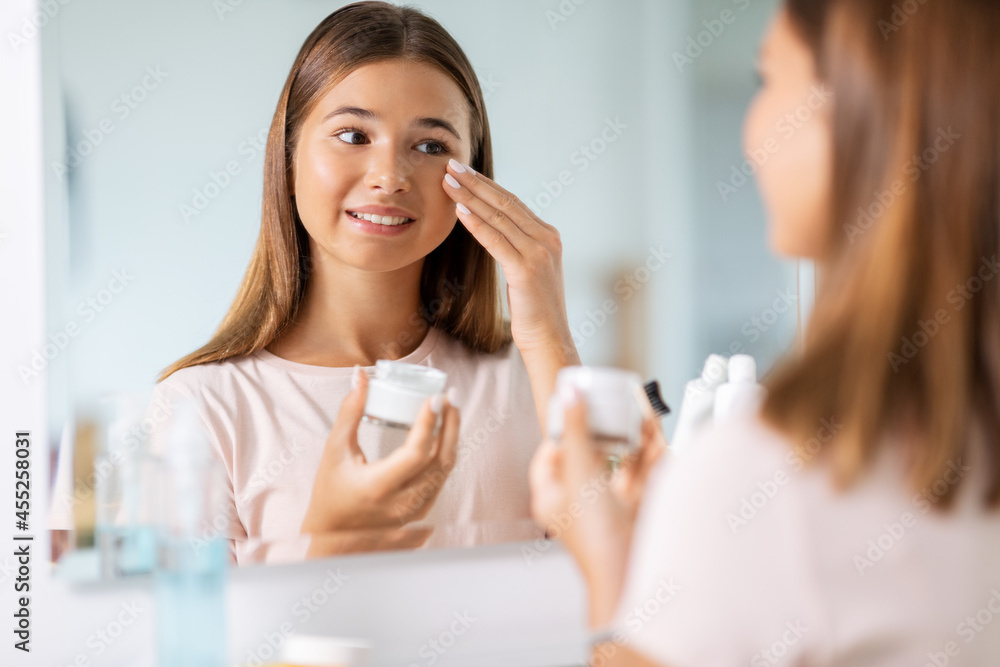 Canvas Prints beauty, hygiene and people concept - teenage girl applying moisturizing cream looking in mirror at bathroom