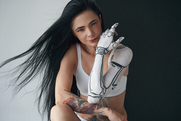 Tattooed woman with robot or cyborg body art wearing lingerie touching her face with her hand