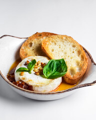 Baked camembert with sauce and toast served in a white bowl over white background. Delicious dinner idea