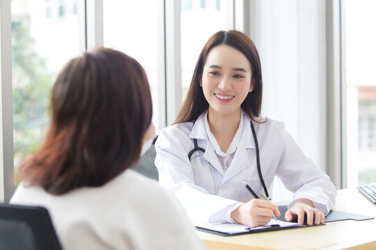 Asian professional doctor female who wears medical coat talks with woman patient to suggest treatment guideline and healthcare concept in office of hospital.