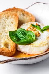 Baked camembert with sauce and toast served in a white bowl over white background. Delicious dinner idea