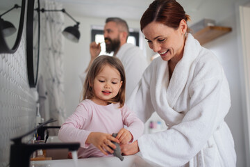 Father and mother with small daughter washing indoors in bathroom in the evening or morning.