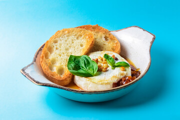 Baked camembert with sauce and toast served in a white bowl over blue background. Delicious dinner idea