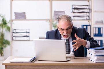 Fototapeta premium Old male employee unhappy with excessive work in the office