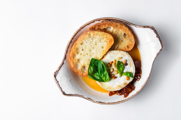 Baked camembert with sauce and toast served in a white bowl over white background. Delicious dinner idea