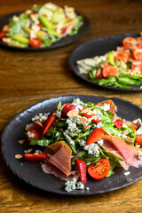 Fresh salad with strawberry, prosciutto, herbs and cheese. Served on a black plate on a rustic wooden table